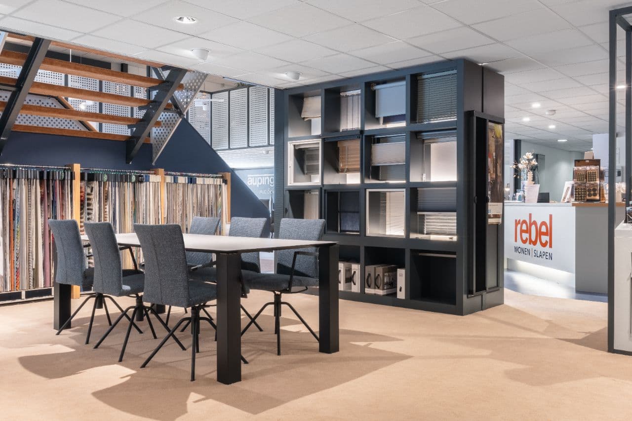 Binnenkijker in de showroom van Rebel Wonen & Slapen in Huizen — raamdecoratie, Auping-hoek, eettafel en de balie met het rebel-logo